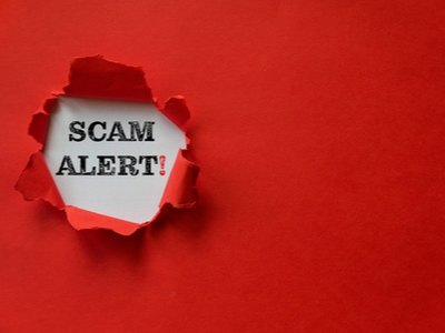 piece of red paper torn open to show the words Scam Alert below